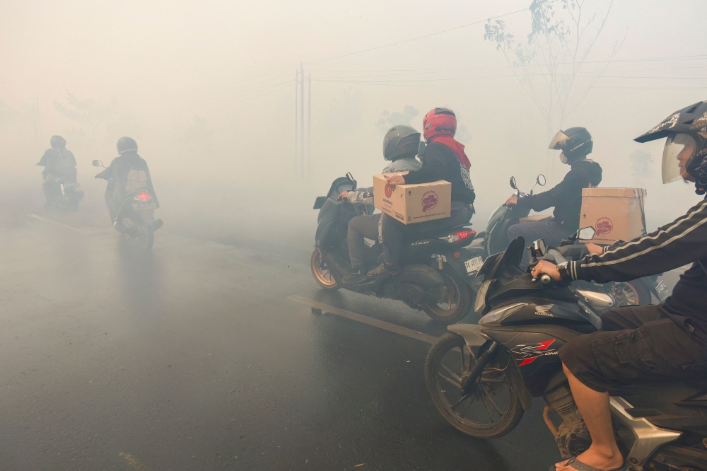 Motorcyclists navigate a road heavily obscured by thick haze from nearby forest and land fires in Tegal Arum, Banjarbaru, South Kalimantan on October 20, 2026. — AFP pic