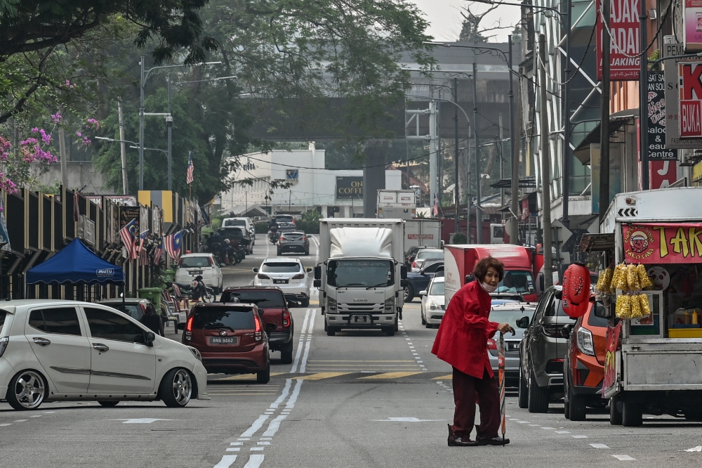 A woman wears a face mask as she walks along a street in Kuala Lumpur on October 19, 2026. — AFP pic 