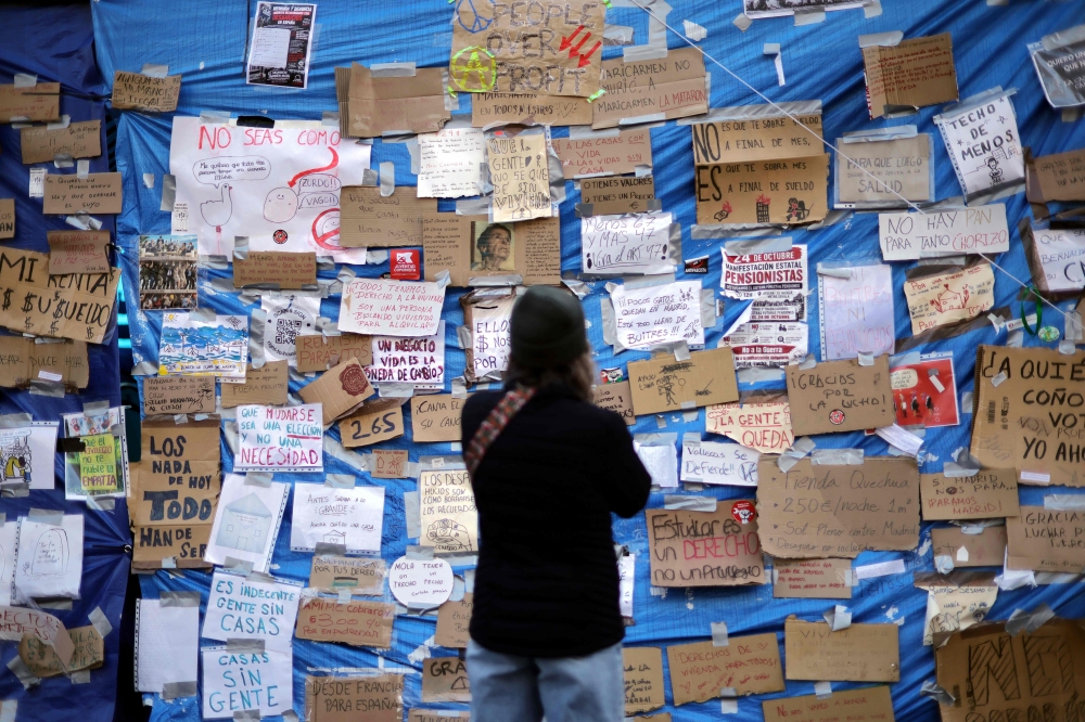A person reads messages displayed on a tarp in a camp set to protest against evictions and the housing crisis in Puerta del Sol square in Madrid October 20, 2026. — AFP pic
