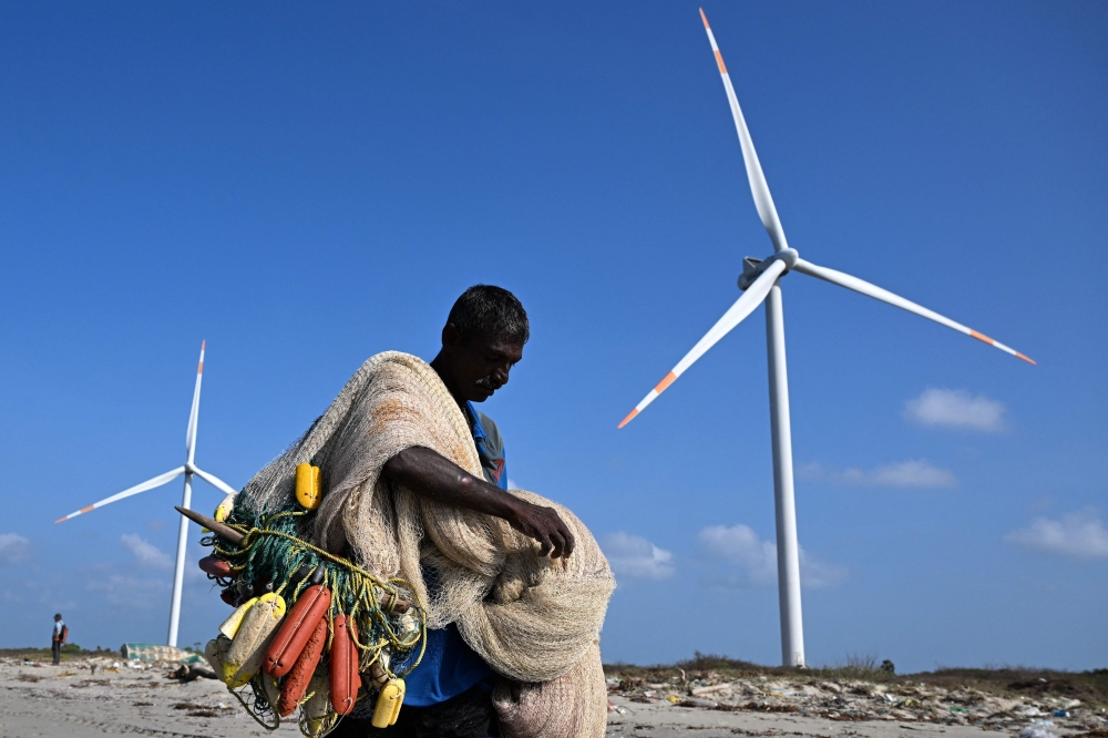 A fisherman carries nets along a beach near a wind power plant on Sri Lanka’s Mannar peninsula on October 3. The government aims to generate 70 per cent of its electricity from renewable sources by 2030 but has frozen new projects in Mannar to ease local opposition. — AFP pic