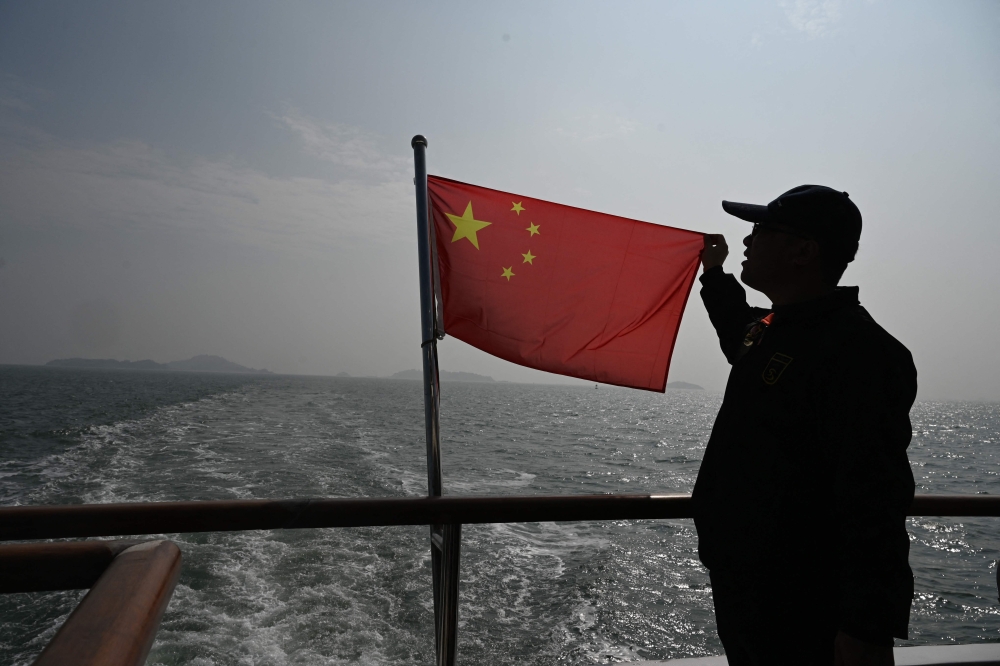 A Chinese man sings as he holds the China national flag in Fujian province on January 11, 2024. — AFP pic