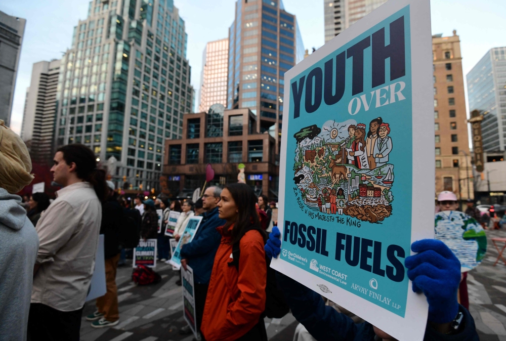 Supporters of the first federal youth climate trial in Canadian history hold up signs during a rally outside the Vancouver Art Gallery in Vancouver October 26, 2026. — AFP pic