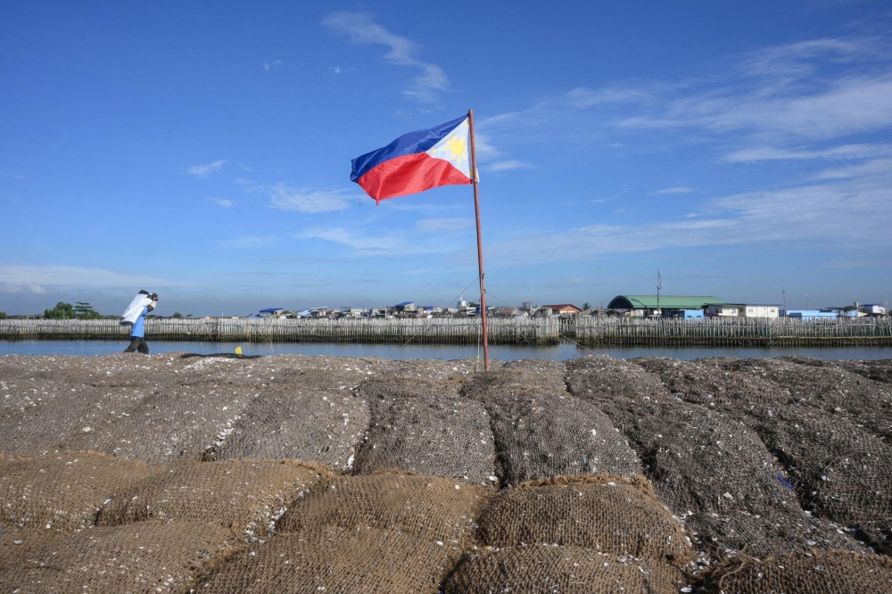 In this photo taken on October 13, 2026, a Philippine flag flutters atop coconut-fibre bags filled with oyster shells on a breakwater at Pamarawan Island in Malolos City, Bulacan province. — AFP pic