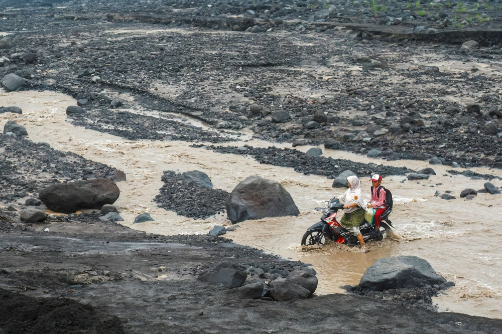 A woman rides a motorcycle with a student across a cold lava flood path from Mount Semeru following heavy rain at Jugosari village, Lumajang, East Java October 29, 2026. — AFP pic
