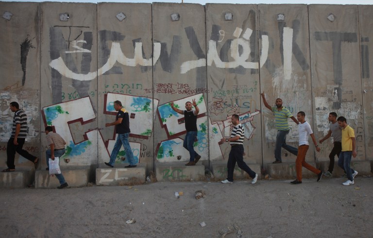 Palestinian youths walk past Israel's controversial separation barrier at the Qalandia checkpoint between Ramallah and Jerusalem, in the occupied West Bank, on August 4, 2013. — AFP pic