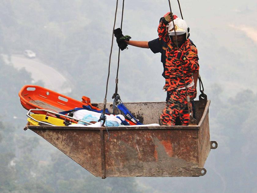 Two rescue personnels using a crane to get down into the ravine in order to bring the victims up. — Picture by Siow Feng Saw