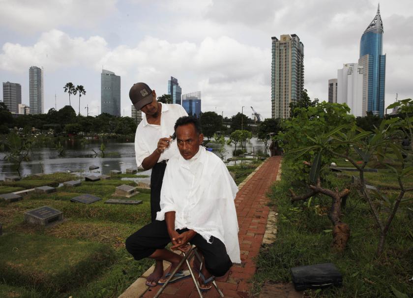 Cemetery worker Mohammad Udin has his hair cut by a mobile barber as the flooded cemetery complex is pictured in the background in Jakarta, January 29, 2014. u00e2u20acu201d Reuters pic