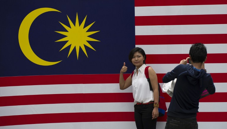 A tourist poses for a picture in front of a national flag ahead of the Malaysiau00e2u20acu2122s 56th Independence Day celebrations in downtown Kuala Lumpur on August 20, 2013. u00e2u20acu201du00c2u00a0AFP pic