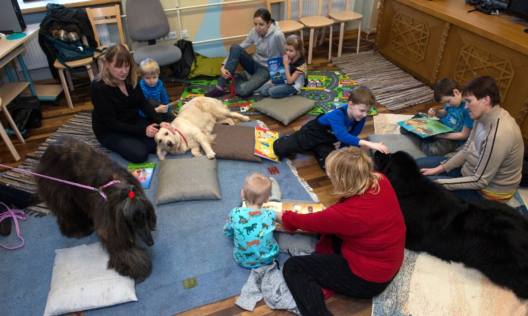 Children read to a dog hired by a library on February 26, 2014 in Tartu, south Estonia to encourage kids to practice reading books aloud, to increase confidence of shy kids. u00e2u20acu201d AFP pic