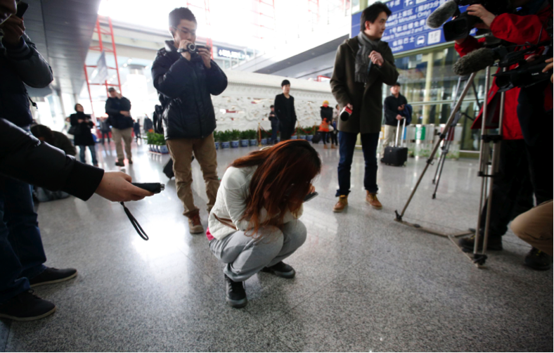 Journalists attempt to interview a woman who is the relative of a passenger on Malaysia Airlines flight MH370, as she crouches on the floor crying, at the Beijing Capital International Airport in Beijing March 8, 2014. — Reuters pic