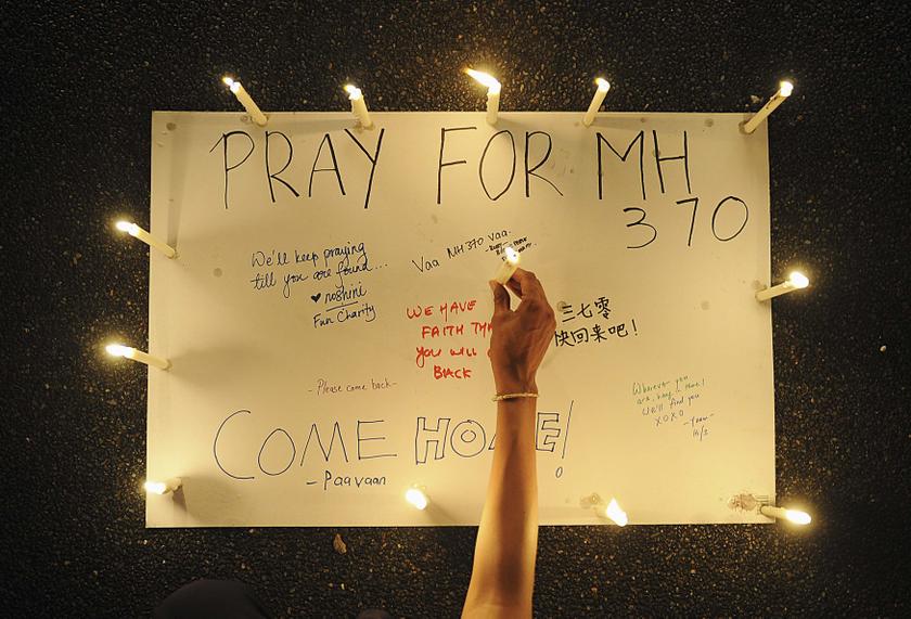 A woman places a lighted candle on a poster with messages expressing hope for passengers of the missing Malaysia Airlines plane MH370 during a candlelight vigil in Petaling Jaya, near Kuala Lumpur March 16, 2014.