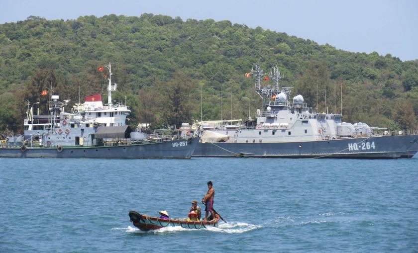 Local residents ride a fishing boat past navy search and rescue ships before the ships depart for the search area for a missing Malaysia Airlines plane, at a port on Vietnamu00e2u20acu2122s Phu Quoc island March 9, 2014. u00e2u20acu201d Reuters pic