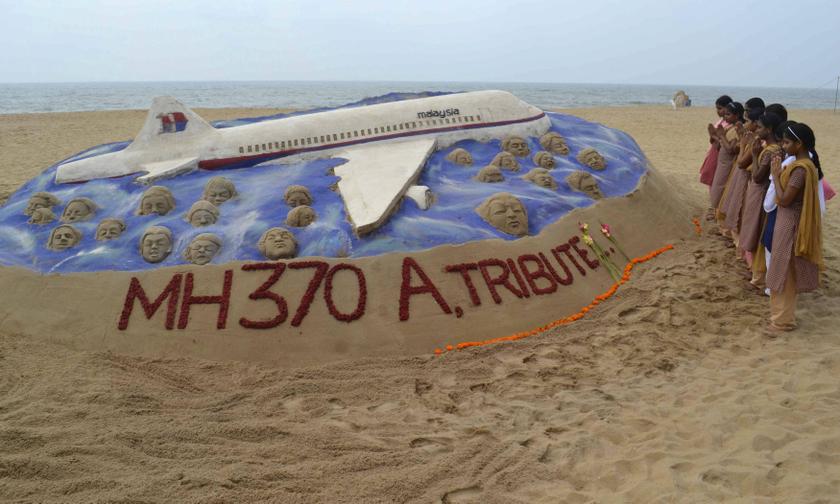Schoolgirls pray next to a sand art sculpture created by Indian sand artist Sudarshan Patnaik to pay tribute to those on board the missing MAS flight MH370, on a beach in Puri, March 25, 2014. u00e2u20acu2022 Reuters picn 