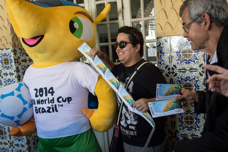 Football fans Joao Bosco (right) and Vanderson Balbino pose with the FIFA World Cup Brazil 2014 mascot, as they show the tickets they bought for the upcoming football tournament after the designated ticketing pick-up centres opened in 12 host cities on Ap
