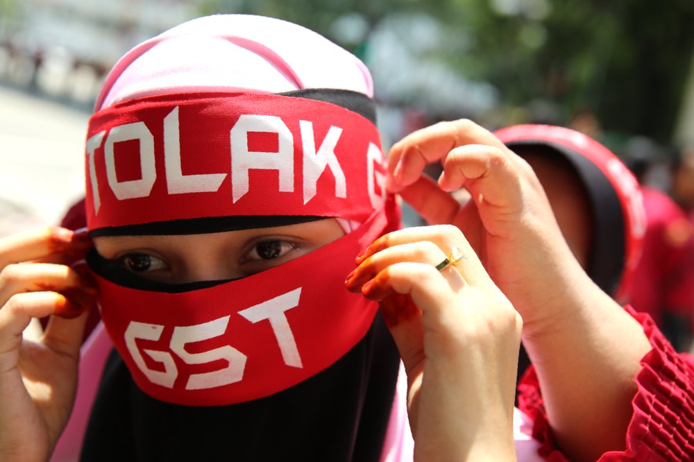 A woman puts on a 'Tolak GST' scarf with the help of friends on May 1, 2014.. u00e2u20acu201d Picture by Choo Choy May