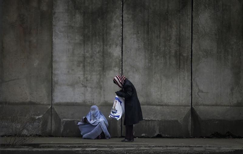 A woman (right) stops to give money to a beggar wearing a burqa outside a police station in Kabul. u00e2u20acu201d Reuters pic