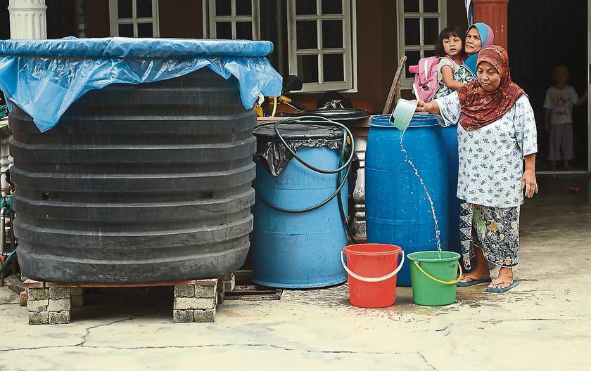 Kuala Langat resident, Zawiah Mokhtar, shares a large water container with her neighbour. u00e2u20acu201d Picture by Ahmad Zamzahuri