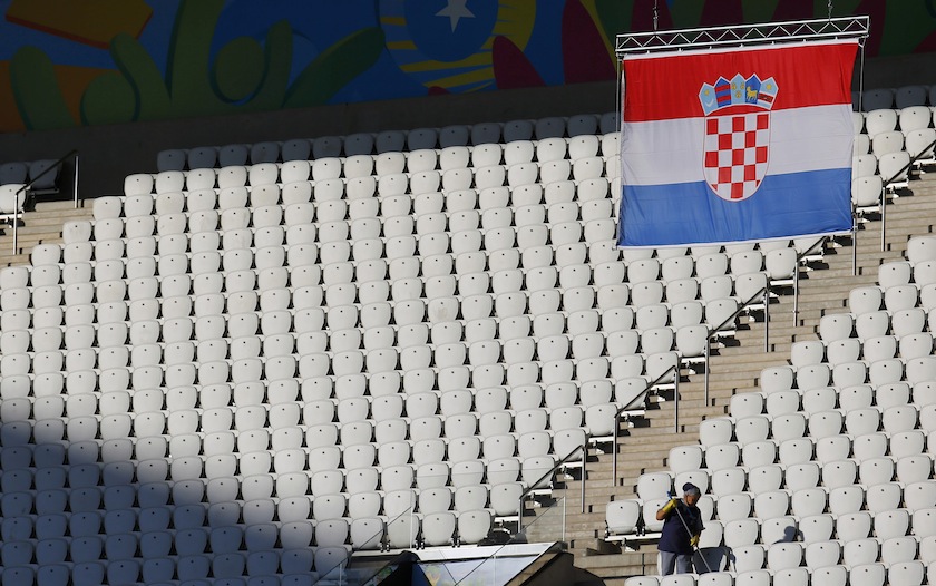 A cleaning lady wipes the seats as the Croatian flag is hoisted up during the Brazilian national team's final practice session at the Arena de Sao Paulo in Sao Paulo, one day before the opening match of the soccer World Cup between Brazil and Croatia, Jun