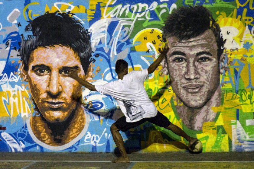 A youngsters plays football in front of a mural of Argentine football player Lionel Messi (left) and Brazil's player Neymar da Silva Santos Junior at a field of Tavares Bastos shantytown (favela) in Rio de Janeiro, Brazil on June 8, 2014. u00e2u20acu201d AFP pic