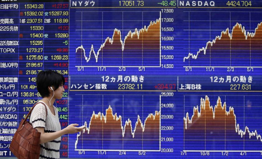 A pedestrian holding her mobile phone looks at an electronic board showing graphs of various countries' stock market indices outside a brokerage in Tokyo July 22, 2014.  u00e2u20acu201d Reuters pic