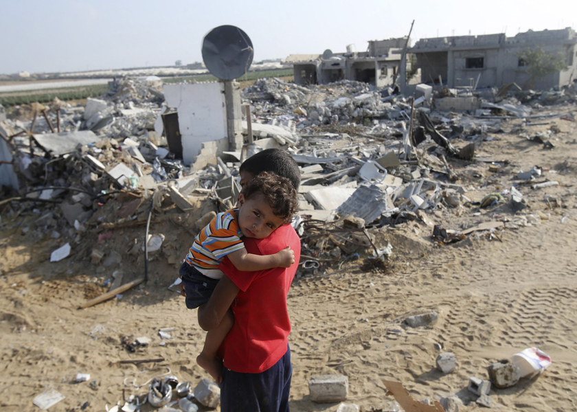 A Palestinian boy carries his brother next to the remains of their house, which witnesses said was destroyed in the Israeli offensive, Gaza Strip, August 13, 2014. — Reuters pic