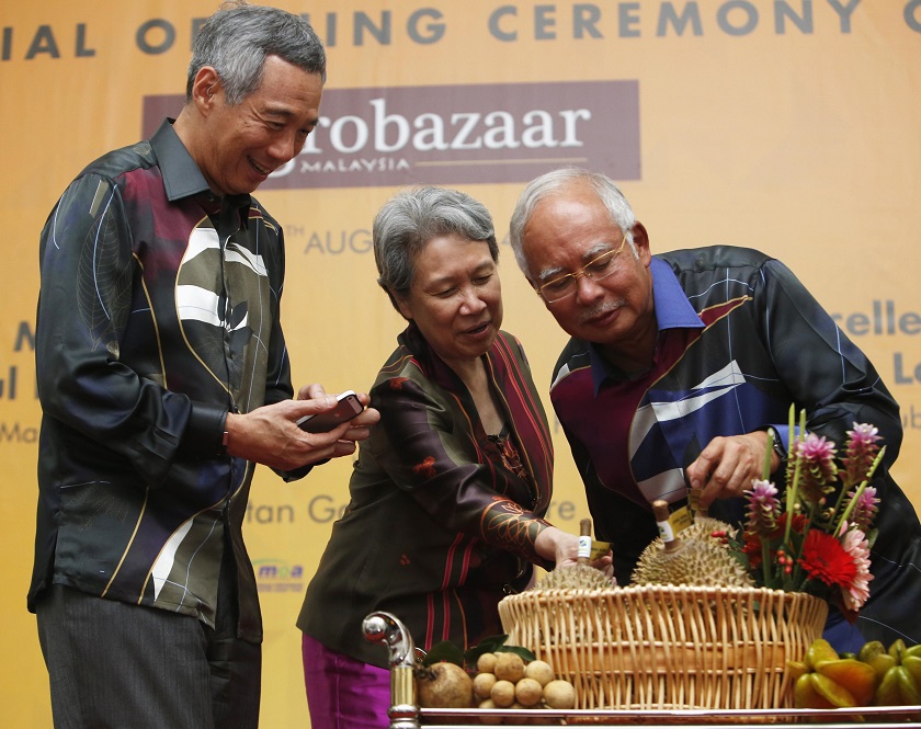 Singaporeu00e2u20acu2122s Prime Minister Lee Hsien Loong takes a picture as he receives a gift of Musang King durians from Malaysian counterpart Najib Razak  next to Leeu00e2u20acu2122s wife Ho Ching as they attend the opening ceremony of Malaysiau00e2u20acu2122s Agrobazaar store in Singapo