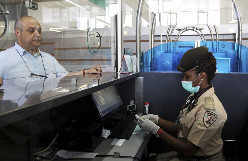 A female Immigration officer wearing a facemask and gloves checks a passenger's passport at the Nnamdi Azikiwe International Airport in Abuja, August 11, 2014. u00e2u20acu201d Reuters pic