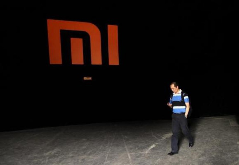 A man checks his mobile phone as he walks past a logo of Xiaomi in Beijing August 16, 2012. u00e2u20acu201d Reuters pic