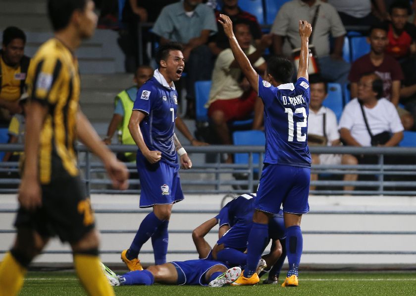Thailandu00e2u20acu2122s Adisak Kraisorn (ground) celebrates with teammates Charyl Yannic Chappuis (L) and Prakit Deeprom (R) after scoring a late goal for Thailand to beat Malaysia in their Suzuki Cup Group B match at Jalan Besar Stadium in Singapore November 26, 20