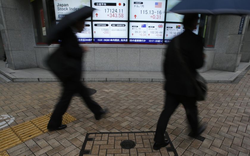 Pedestrians with umbrellas walk past an electronic board showing Japan's Nikkei average (top middle left) and the exchange rates between the Japanese yen and the US dollar (top middle right), outside a brokerage in Tokyo, November 21, 2014. u00e2u20acu2022 Reuters pi