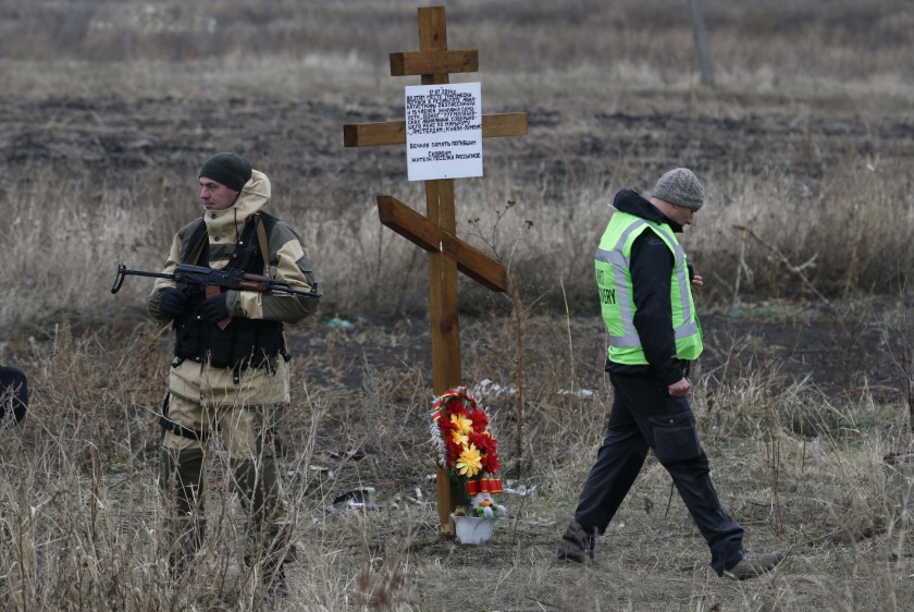 A member of the recovery team works at the site where the downed flight MH17 plane crashed near the village of Rozsypne as an armed security representing the self-proclaimed Donetsk People's Republic stands guard near a cross erected by local residents in