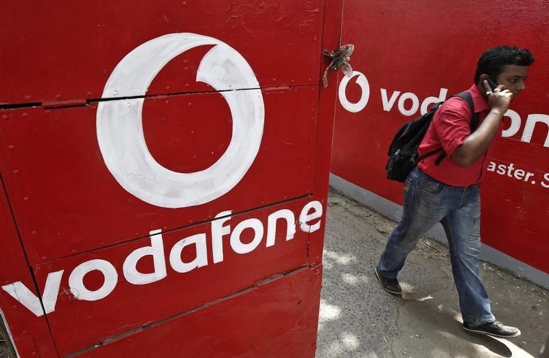 A man speaks on his mobile phone as he walks past logos of Vodafone painted on a roadside wall in Kolkata May 20, 2014. u00e2u20acu201d Reuters pic