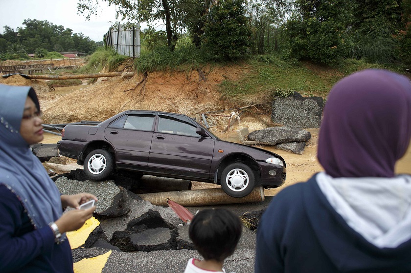 People stand next to a car as it sits on a road damaged by flooding at Kuala Krai in Kelantan December 30, 2014. — Reuters pic