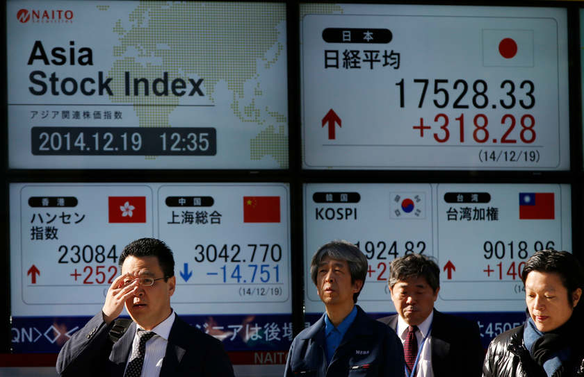 Passersby walk past an electronic board showing Japan's Nikkei share average (top right) and Asian countries' stock indexes outside a brokerage in Tokyo December 19, 2014. u00e2u20acu201d Reuters pic