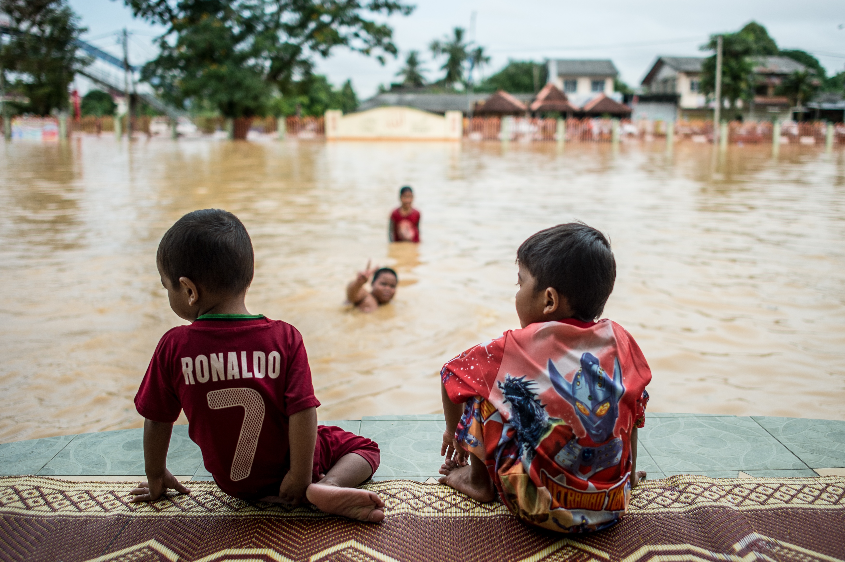 Two boys look on as their friends play in floodwaters in Pengkalan Chepa, near Kota Baru on December 28, 2014. u00e2u20acu201d AFP pic