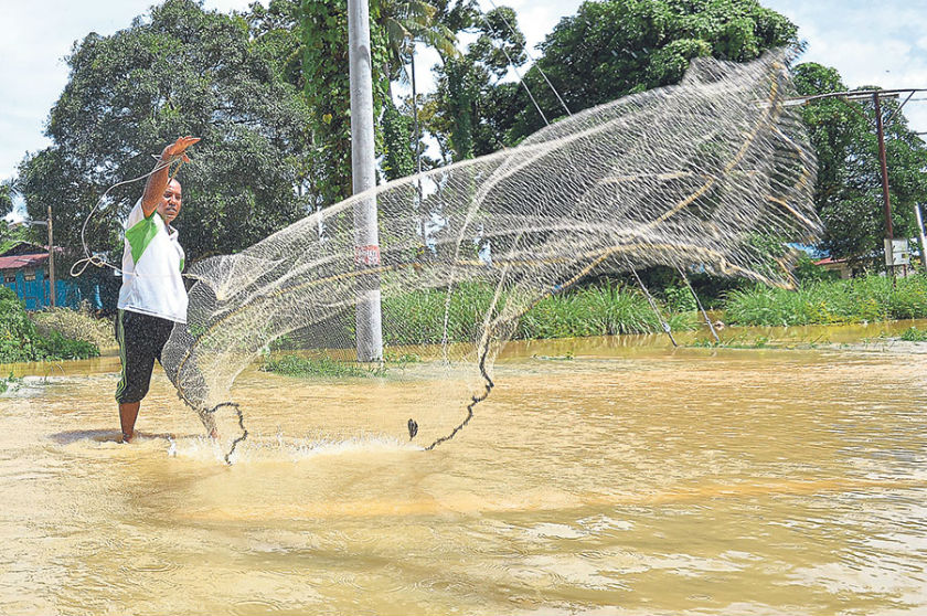 Nizam casts his net into a flooded road in Kampung Teluk Kepayang. u00e2u20acu201d Picture by Marcus Pheong