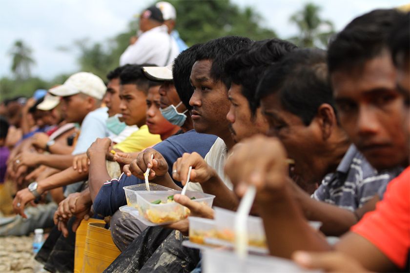 Manek Urai residents are seen resting for their lunch meal of rice and vegetarian dishes cooked by local women in a makeshift kitchen.