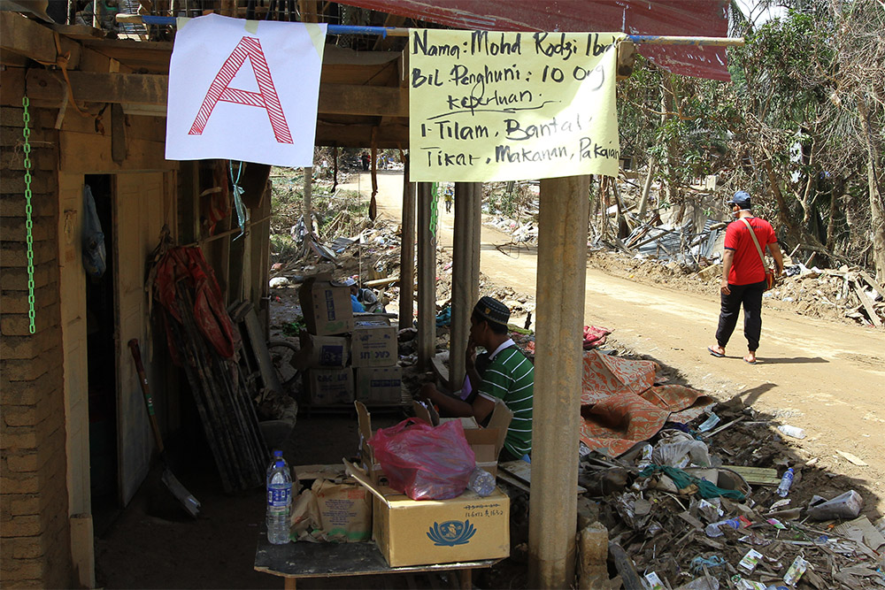 A flimsy yellow manila card hangs from a pole under a tin roof in flood-ravaged Kg Manek Urai Lama, declaring to all passers-by in Malay: 'Mohd Rodzi Ibrahim. Residents: 10 people. Needs: Mattresses, pillows, food, clothes'. — Picture by Yusof Mat Isa 