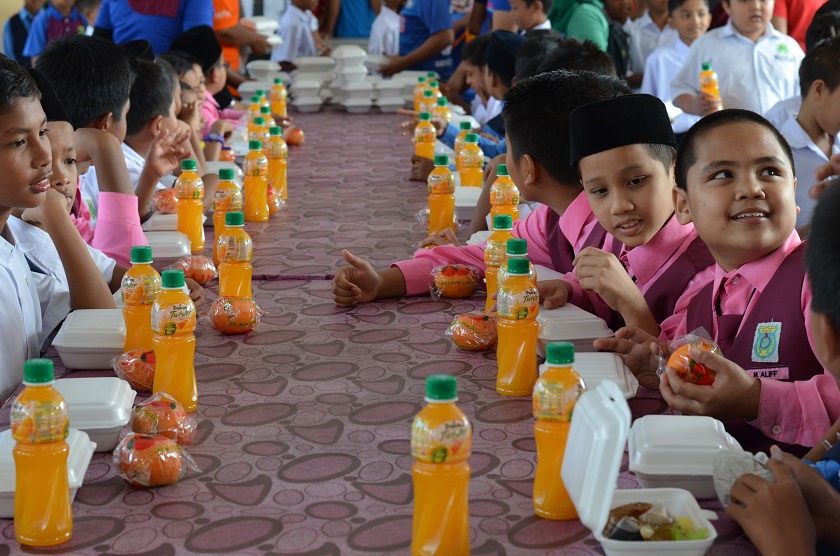 A student at SK Seberang Pasir Mas receives a mandarin orange from volunteers, while his friend excitedly peeps at the rare treat of chicken rice.