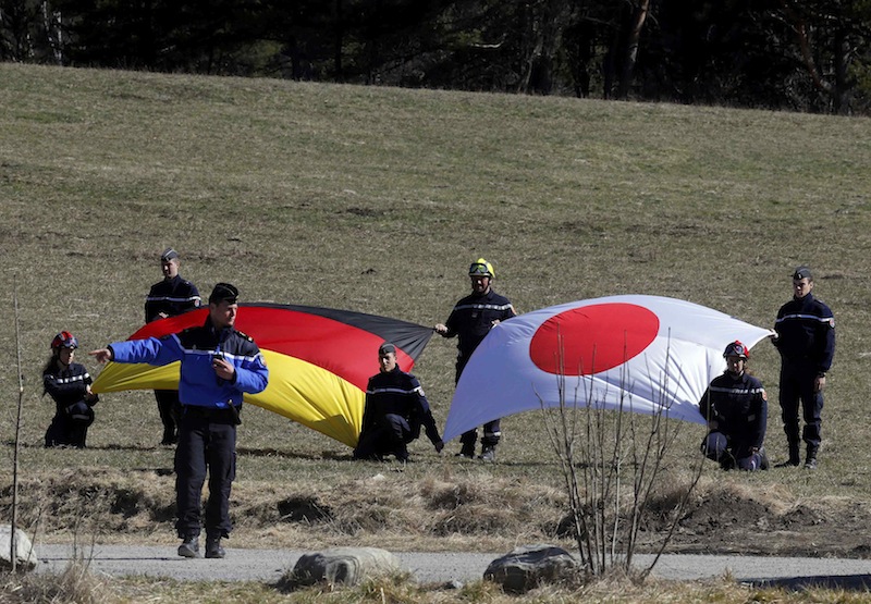 French rescue workers hold Germany's and Japan's flags during a ceremony in tribute to the Japanese victims at the memorial for the victims of the air disaster in the village of Le Vernet, near the crash site of the Germanwings Airbus A320 in French Alps,