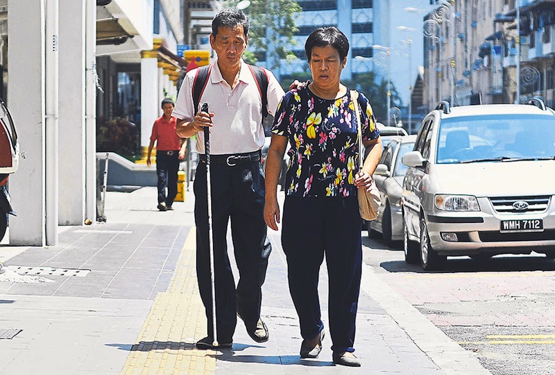 Eg and Ooi walk along the yellow track. They say they still face difficulties despite using the facilities for the visually impaired.