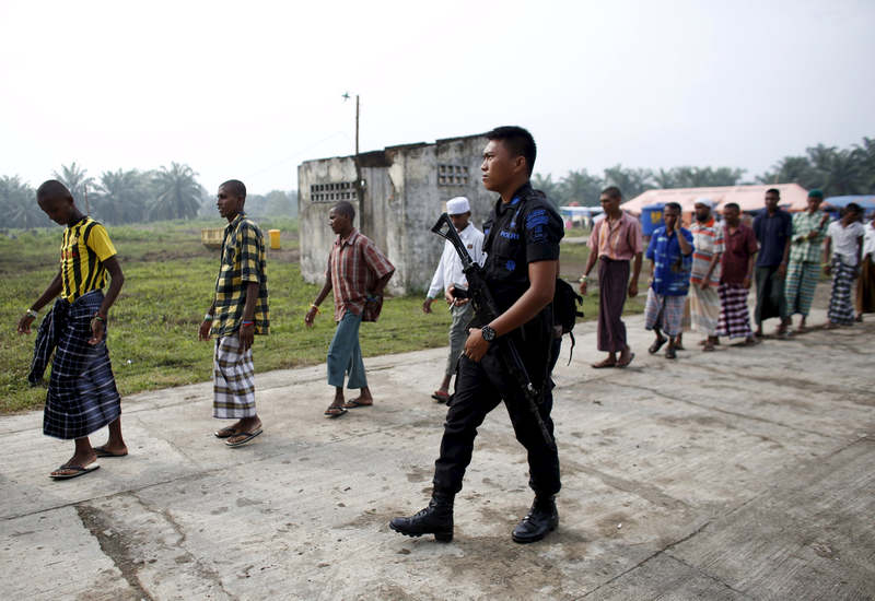 An Indonesian police officer walks beside Rohingya migrants as they walk to collect breakfast at a temporary shelter in Aceh Timur regency, Indonesia May 27, 2015. u00e2u20acu201d Reuters pic