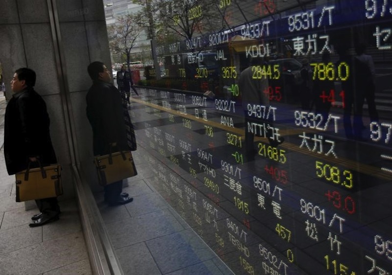 A man hides from the rain in front of an electronic stock quotation board outside a brokerage in Tokyo April 7, 2015.u00c2u00a0u00e2u20acu201d Reuters pic