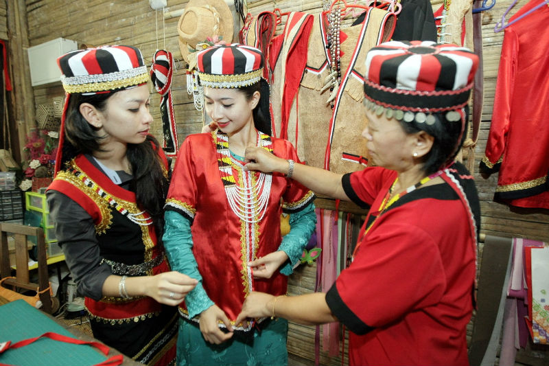 Nazarida Kamal (centre) and Dalila Dayana (left) try out Bidayuh traditional costume at the Sarawak Cultural Village, Kuching. Traditional clothing is worn by the Bidayuh during Gawai Dayak Day celebrated on June 1. u00e2u20acu201d Bernama pic