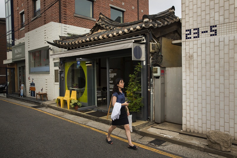 A woman walks past a restored hanok, a traditional house with wood frame a and curving tiled roof, in the Samcheong neighbourhood of Seoul, South Korea, July 7, 2015.
