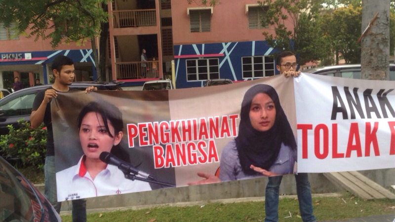 A banner labelling Dyana Sofya Mohd Daud and Syefura Othman as 'traitors to the race' is held by a small group of protesters outside a DAP buka puasa event in Shah Alam on July 10, 2015. — Picture courtesy of Yeo Bee Yin