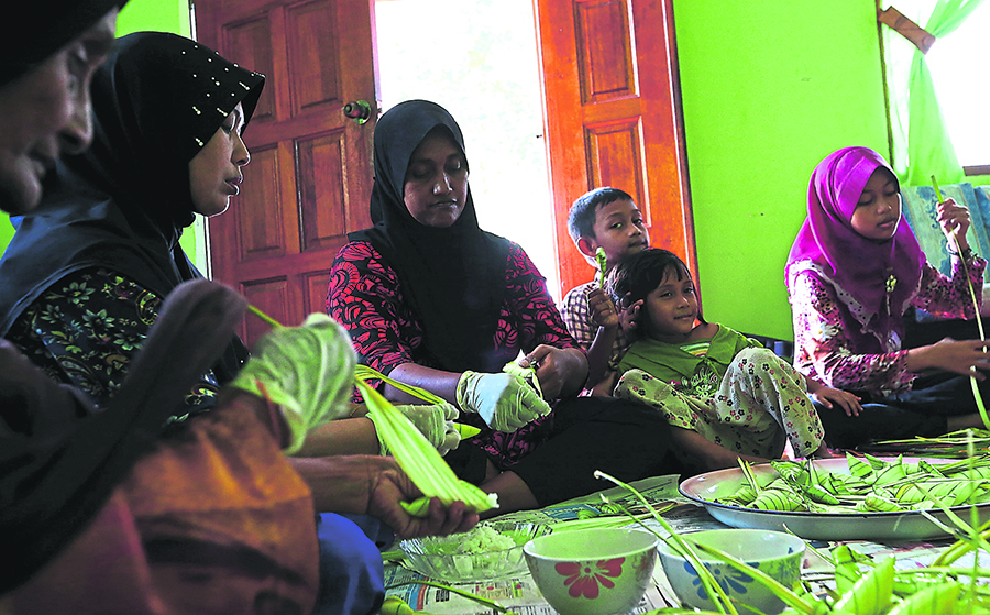 Rosmina Mohd Yusof (second from left), daughter Zabedah (right) and sister-in-law Radziah Ahmad insert glutinous rice into palas leaves to make nu00e2u20acu02dcketupat palasu00e2u20acu2122 at her home at Permatang Pak Elong, Kepala Batas, Penang. u00e2u20acu201d Picture by Sayuti Zainudin