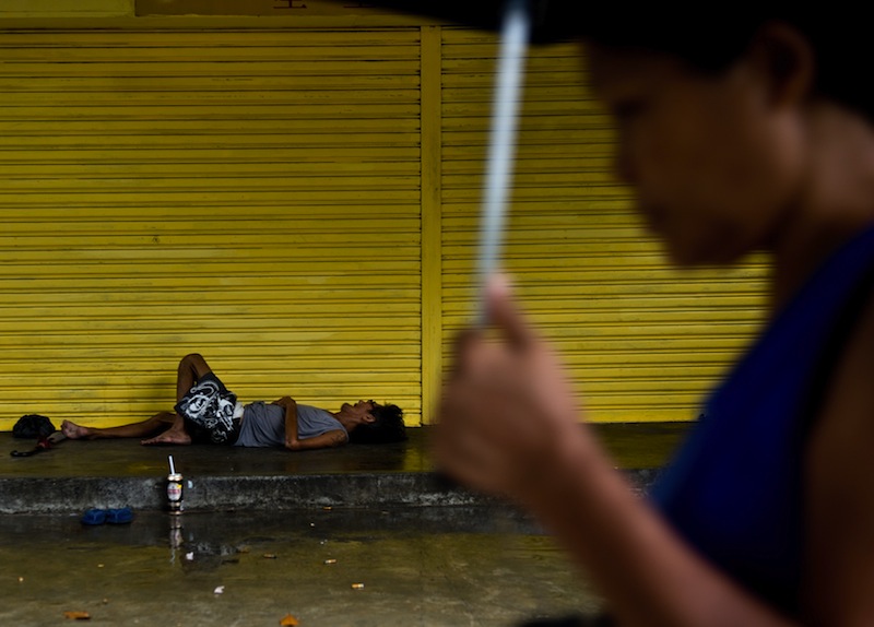 A homeless man sleeps on a pavement as a Malaysian woman carries an umbrella during a rain-shower in downtown Kuala Lumpur on June 2, 2015. u00e2u20acu201d AFP pic