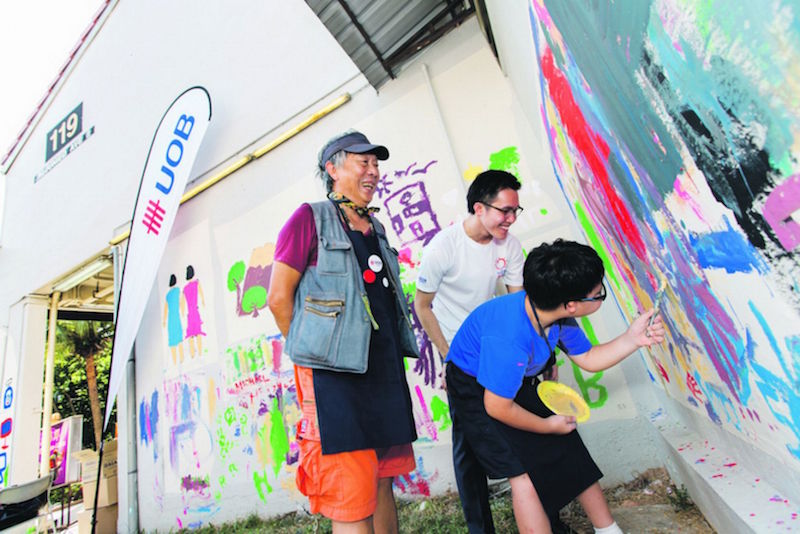 Cultural Medallion recipient Goh Beng Kwan assisting special needs students at a mural painting session at Aljunied for UOB, for which he had also won the first UOB Painting Of The Year award. — Picture by UOB via TODAY