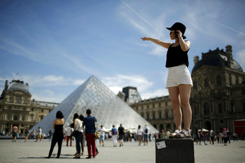 A tourist poses for a souvenir picture near the Pyramid of the Louvre Museum in Paris, France, August 1, 2015. France has been the world's most visited country since the 1980s, welcoming 84 million tourists last year. u00e2u20acu201d Reuters pic